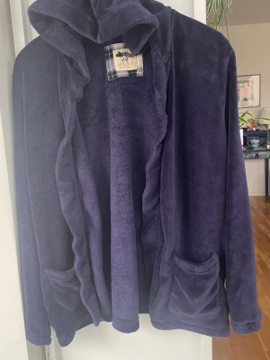 Mörklblå morgonrock från H&M - Mysig mörkblå morgonrock i kort modell från H&M i mjuk fleece. Modellen har huva, två framfickor och en öppen design med knytband. Perfekt för att chilla hemma och hålla sig varm under kalla morgnar.