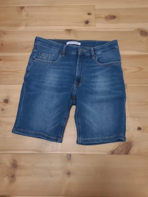 Blå jeansshorts från Calvin Klein - Snygga blå jeansshorts från Calvin Klein Jeans med klassisk femficksdesign och gul kontrastsöm. Shortsen har normal passform och är tillverkade i bomull. Perfekta för sommaren och ger en avslappnad look.