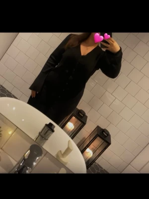 Svart klänning med knappar - Viral svart långklänning med v-ringning och långa ärmar. Klänningen har knappar framtill. 