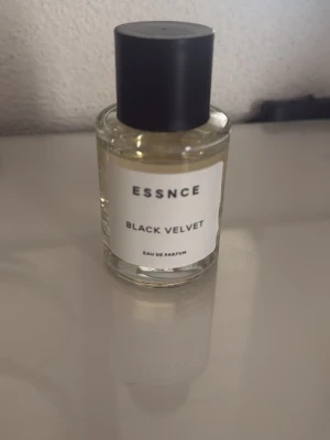 Essnce Black Velvet Eau de Parfum - Essnce Black Velvet Eau de Parfum kommer i en stilren, rund glasflaska med svart lock. Doften är elegant och flaskan har en minimalistisk vit etikett med svart text. Perfekt för dig som gillar snygg och enkel design på parfymflaskor.