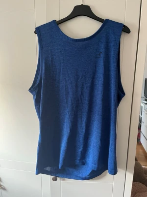 Träningslinne - Snygg blå ärmlös träningslinne med rund halsringning. Perfekt för träning eller varma dagar. Tunt och lätt material som andas. Enkel och stilren design med liten logga på bröstet.