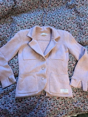 Ljusrosa stickad cardiganjacka - Säljer en ljusrosa kofta från Odd Molly med fyra fickor, dekorativ rosett vid ärmslut och klassisk krage. Koftan har tre knappar framtill och en snygg etikett på ena fickan. Perfekt för dig som gillar en söt och stilren look.