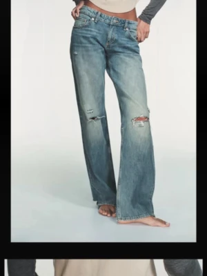 Blå slitna baggy Zara jeans  - Säljer ett par blå baggy jeans med slitningar och hål på knäna och baksidan. Klippta längst mer och har en liten slits.