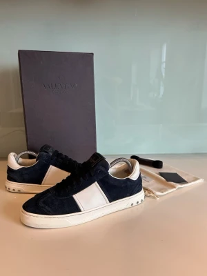 Valentino Flycrew - Valentino Flycrew i mörkblå mocka. Skorna är använda men i riktigt bra skick. Skora har alla nitar kvar och helt nya innersulor. Skorna levereras med originalkartong, dustbag, extra skosnören och tillbehör. Storlek 40,5 men sitter större. Hela vägen upp mot 42 enligt mig. Bara att höra av er om ni har frågor om pris eller tankar om mått.