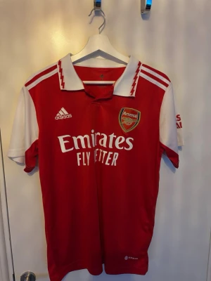 Arsenal matchtröja Adidas Saka #7 - Röd och vit Arsenal matchtröja från Adidas med Saka och nummer 7 på ryggen. 