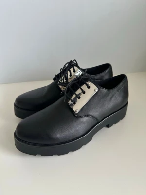 Svarta Vagabond skor, 100% äkta skinn, 36 - Klassiska svarta snörskor / skor / brogueskor från Vagabond i storlek 36. Modern platåsula och silverfärgade detaljer vid snörningen. Tidlös modell med uppstyltade detaljer. 100% äkta skinn / läder. Mycket gott skick, som nya!   (Kan även hämtas vid behov, i Stockholm)