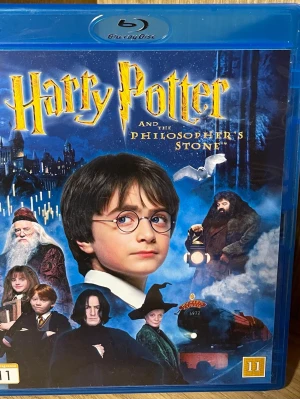 Harry Potter and the Philosopher's Stone Blu-Ray  - Säljer en Blu-ray utgåva av Harry Potter and the Philosopher's Stone. Omslaget är blått med magiska motiv och ikoniska karaktärer från filmen. Filmen är på engelska och har svensk text, med extra material och Dolby-ljud. Perfekt för fantasyälskare.