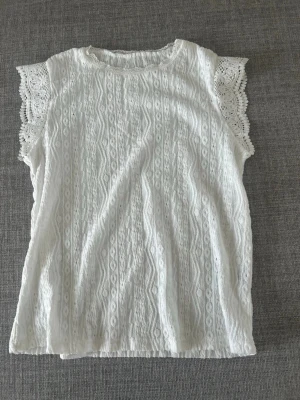 Vit spetsblus med kort ärm - Söt vit blus med spetsdetaljer och korta ärmar. Blusen har ett vackert spetsmönster över hela plagget och extra dekorativa spetskanter vid ärmarna. Perfekt för dig som gillar romantisk och feminin stil. Det finns ingen lapp men passar xs-s💕💕