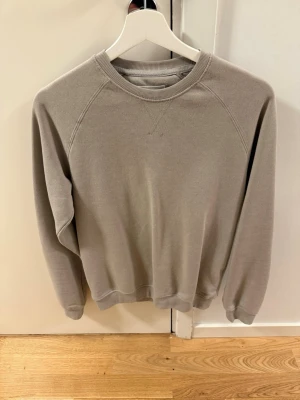 Beige basic sweatshirt - En enkel beige sweatshirt med rund halsringning och raglanärmar. Tröjan har ribbade muddar vid ärmslut och nederkant för en clean look. Perfekt för dig som gillar minimalistisk stil och vill ha något bekvämt i garderoben. Materialet ser ut att vara mjuk bomullsblandning.