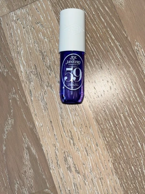 Sol de Janeiro 59 Parfym Mist - Sol de Janeiro 59 är en parfym mist i en snygg lila glasflaska med vit plastkork. Flaskan har en modern, rundad form och tydlig logga framtill. Perfekt för dig som vill ha en fräsch och unik doft i din samling.