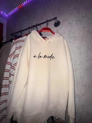 Vit hoodie från Amisu med tryck - Snygg vit hoodie från Amisu med svart text 'à la mode' på bröstet. Hoodien har huva med dragsko och är tillverkad i mjukt material som känns skönt mot huden. Perfekt för en avslappnad och trendig look.