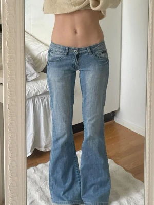Blå bootcut jeans med låg midja - Säljer ett par ljusblå bootcut jeans med låg midja och slitna detaljer. Jeansen har klassiska fem fickor, dubbla knappar och utsvängda ben. Perfekta för en avslappnad och trendig look. Passar xs och jag är 166 cm ❤️