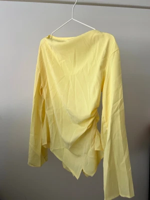 Gul långärmad topp med asymmetrisk kant - Trendig gul långärmad topp med asymmetrisk nederkant och lös passform. Toppen har en enkel design utan synliga detaljer och är perfekt för dig som gillar färg. Tillverkad i ett lätt och mjukt material.