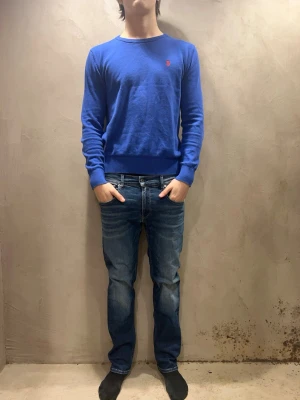 Blå raka jeans från replay - Snygga blå jeans från replay med klassisk femficksmodell och raka ben. Jeansen har en tvättad look med subtila slitningar och kontrastsömmar. Tillverkade i denim med skinnpatch bak i midjan. Perfekta för en avslappnad och trendig stil.