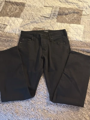 Svarta jeans från Jack and Jones - Säljer ett par svarta jeans i storlek 33/30. Klassisk femficksmodell med raka ben och knappgylf. Jeansen är tillverkade i ett mjukt bomullsmaterial med lite stretch för extra komfort. Perfekta till en avslappnad och stilren look.