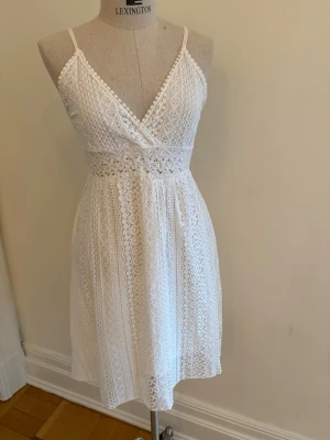 Vit spetsklänning med smala axelband - Superfin vit klänning med spetsdetaljer. Klänningen har smala axelband och markerad midja. Perfekt för sommarens alla tillfällen och ger en romantisk känsla.