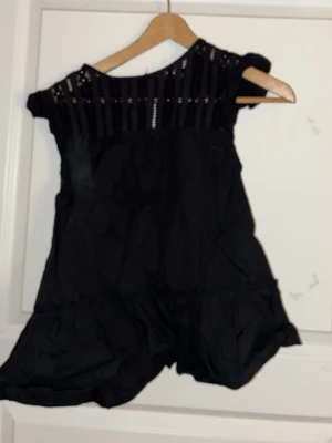 Svart blus med spetsdetaljer - Snygg svart blus . Överdelen har fina spetsdetaljer och små hål längs axlarna för en trendig look. Perfekt för dig som vill ha en stilren och bekväm outfit. Materialet känns lätt och luftigt.