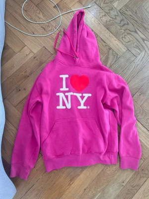 Rosa I ❤️ NY hoodie - Säljer en rosa hoodie med den klassiska I ❤️ NY-loggan tryckt framtill.Köpt i New York  Otroligt skön och jättebra skick  Materialet på insidan är fortfarande fluffigt då  den knappt använts, så den är så gott som ny.   S/XS vet inte riktigt men passar mig, för referens är jag 162 och brukar bära xs.   Hoodien har huva med dragsko och en stor magficka. Tillverkad i mjukt bomullsmaterial och har ribbade muddar vid ärmslut oc