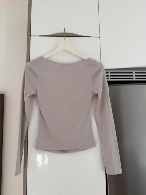 Beige långärmad topp med öppen rygg - Säljer en stilren beige långärmad topp med öppen rygg och bred urringning. Toppen har en tight passform och är tillverkad i ett mjukt, stretchigt material som känns skönt mot huden. Perfekt att matcha med jeans eller kjol för en trendig look.