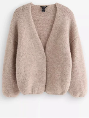 Beige stickad kofta från Lindex - Mysig beige stickad kofta från Linexs med ballongärmar och djup V-ringning. Koftan är gjord i ett mjukt, fluffigt material och har en avslappnad passform utan knappar. Perfekt att slänga över en topp för extra värme.