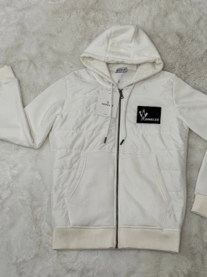 Vit hoodie från Moncler med dragkedja - Snygg vit hoodie från Moncler med dragkedja framtill och svart logotyp-patch på bröstet. 