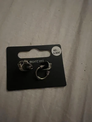 Silvriga hoops från Montini - Säljer ett par silvriga hoop-örhängen från Montini. De har en cool design med små detaljer i form av lindade metalltrådar runt ringen. Perfekta för dig som gillar en stilren men ändå edgy look.