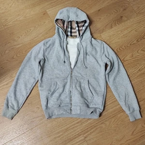 Grå Burberry hoodie - Säljer en grå Burberry zip up hoodie med rutigt foder i huvan och loggo på bröstet.