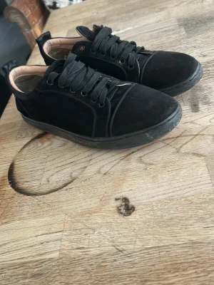 Svarta låga sneakers i mocka - Snygga svarta sneakers i mocka med matchande svarta skosnören och diskreta sömmar. Skorna har en låg profil och en klassisk siluett som passar till det mesta. Insidan är ljusbeige och sulan är svart. Perfekta för en clean och stilren look. Lite sliten på sulan där texten har försvunnit lite av användning passar 39/40
