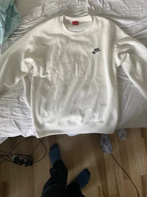 Bra Fejk Vit Nike sweatshirt med logga - Säljer en stilren vit sweatshirt från Nike med klassisk svart logga broderad på bröstet. Tröjan har rund halsringning, långa ärmar och ribbade muddar. Perfekt för en clean och sportig look.