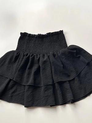 Svart volangkjol med smock - Kort svart kjol med bred smock i midjan och dubbla volanglager.  Stretchigt material