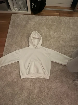 Vit hoodie - Säljer en stilren vit hoodie med croppad passform och stor huva. Hoodien har en klassisk magficka framtill och ribbade muddar vid ärmslut och nederkant. Perfekt för en avslappnad och trendig look. Materialet känns mjukt och bekvämt. Tröjan har några fläckar på sig.