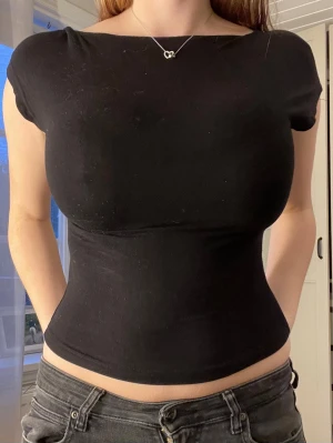 Svart croppad topp med kort ärm - Säljer en svart, croppad topp med korta ärmar och rund hals. Öppen i ryggen och tunt elastiskt material så skön att ha på sommaren. Tröjan är dock från SHEIN 