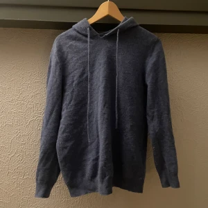 Ljus blå merinoull hoodie - Säljer en stilren ljusblå hoodie med långa ärmar och justerbar huva. Perfekt för kyliga dagar och enkel att matcha med andra plagg. Mjuk och bekväm att bära.