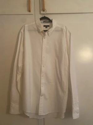 Gant skjorta - Klassisk vit skjorta från gant med lång ärm och knappar framtill. Skjortan har en enkel och stilren design med button-down krage och är tillverkad i bomull för en skön känsla. Perfekt till alla tillfällen där du vill vara lite extra snygg.