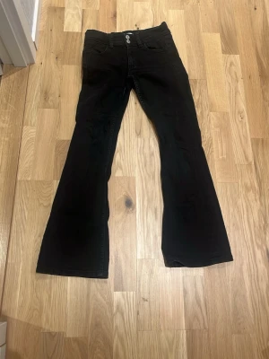 Svarta bootcut jeans med hög midja - Säljer ett par svarta bootcut jeans med hög midja och klassiska fem fickor. Jeansen har utsvängda ben och dubbla knappar i midjan. Perfekta för dig som gillar en retroinspirerad look och vill ha ett par jeans som sticker ut.