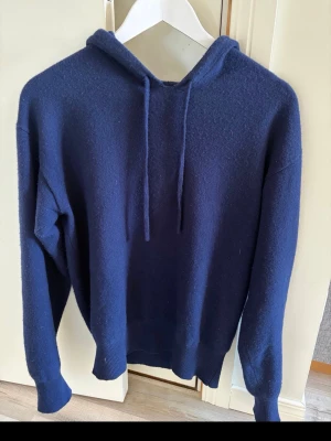 Mörkblå hoodie från Carmès - Mysig mörkblå hoodie från Carmès i storlek M. (Passar S, XS ) Klassisk modell med huva och dragsnören, ribbade muddar vid ärmslut och nederkant. Perfekt för en avslappnad och stilren look. Materialet känns mjukt och bekvämt mot huden. 