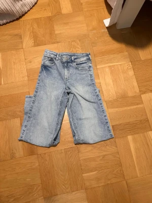Ljusblåa raka jeans med hög midja 128-132 - Säljer ett par ljusblå jeans med raka ben och hög midja. Jeansen har klassisk femficksdesign och är gjorda i ett mjukt denimtyg. Perfekta för en avslappnad och trendig look. OBS det är ett barn plagg för barn som är 131 cm ungefär