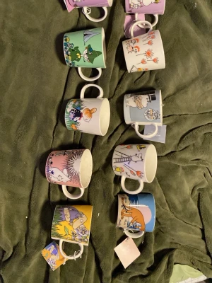 Muminmuggar samling Arabia - Samling med tio färgglada Muminmuggar från Arabia, alla med olika motiv från Mumindalen. Muggarna har olika färger som lila, grön, blå, gul och rosa, och varje mugg har unika illustrationer av Muminfigurer. Perfekt för dig som älskar Mumin och vill ha en rolig samling. Säljer 150 kroner styck , 