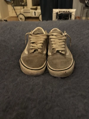 Beige Vans Old Skool sneakers - Säljer ett par klassiska Vans Old Skool sneakers i beige med vit sidostripe och gummisula. Skorna har lågt skaft, snörning och är tillverkade i en mix av mocka och canvas. Perfekta för dig som gillar en avslappnad och tidlös stil. Väldigt slitna. 