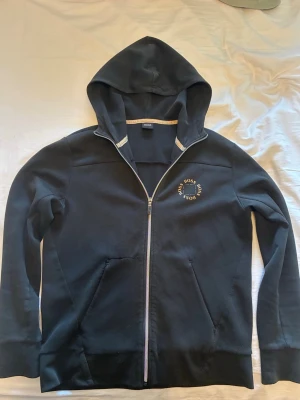 Svart zip hoodie från Hugo Boss - Köptes för några år sen använder inte längre. Har en defekt vid ena fickan där den gick sönder förut men är ihop sydd igen (sista bilden) därav varför priset är billigare. Pris kan diskuteras.