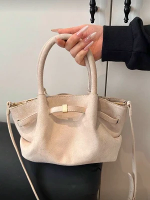 Beige mocka handväska med axelrem - Stilren beige handväska i mjuk mocka med dubbla handtag och avtagbar axelrem. Väskan har guldfärgade detaljer och en elegant, något slouchy form. Perfekt för dig som gillar minimalistisk och trendig design.