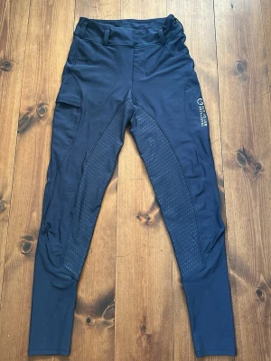 Mörkblåa ridbyxor - Snygga mörkblå ridbyxor från Equestrian Way of Life med helskoning i silikon, bälteshällor och mobilficka på vänstra ben. Ridbyxorna är använda enbart några fåtal gånger och är därför iprincip i nyskick. De är i barnstorlek L men skulle säga att de motsvarar en vuxenstorlek XS.