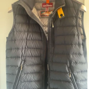 Svart dunväst från Parajumpers - Snygg svart  dunväst från Parajumpers med gul detalj vid kragen och två dragkedjeförsedda fickor framtill. Västen har en quiltad design och hög krage, perfekt för lager-på-lager-stil. Materialet är lätt och isolerande dun.