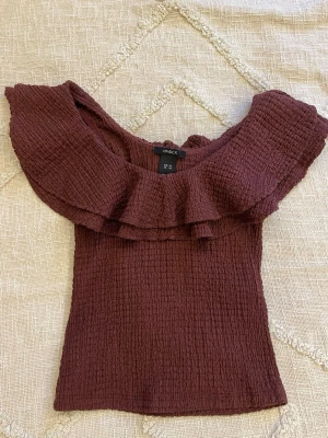 Vinröd volangtopp från Lindex - Supersöt vinröd topp från Lindex med volang runt axlarna och offshoulder-design. Toppen är gjord i ett strukturerat, stretchigt tyg som sitter snyggt på kroppen. Perfekt för dig som vill sticka ut lite extra med en trendig look. Använd en gång, inga defekter alls.