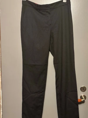 Svarta kostymbyxor med smal rand - Säljer ett par svarta kostymbyxor med diskreta smala kritstreck. Klassisk rak passform och knappgylf. Perfekta för en stilren look och passar till skjorta eller kavaj. 