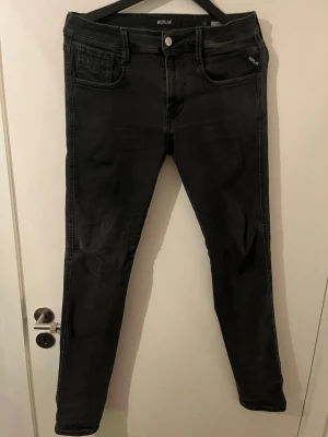 Svarta slim jeans från Replay - Snygga svarta slim jeans från Replay med klassisk femficksdesign och silverfärgad knapp. Jeansen är tillverkade i stretchigt material för extra komfort. Perfekta för en trendig och avslappnad look.