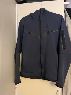 Mörkblå Nike tech fleece hela dressen  - Hej! Säljer min blåa Nike tech fleece då jag inte använder den. Den har legat i garderoben i 2 år ungefär så hade varit skön att bli av med den. Så skulle du vara intresserad hör av dig!🫡 tröjan är i storlek S och byxorna är i storlek L 