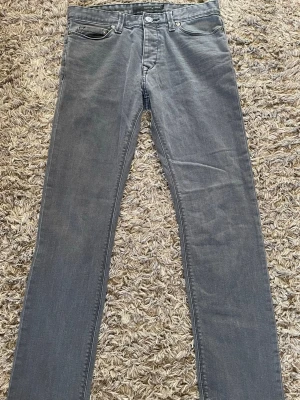 Calvin Klein Jeans - Snygga grå jeans från Calvin Klein Jeans med klassisk femficksdesign och raka ben. Jeansen har metallknapp med logotyp och är tillverkade i denim. Perfekt för dig som vill ha en stilren och tidlös look.