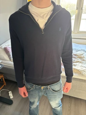 Mörkblå halvzip från Ralph Lauren - Snygg mörkblå tröja från Ralph Lauren med halvzip och diskret logga på bröstet. Tröjan har långa ärmar, ribbade muddar och en klassisk passform. Perfekt att bära över en t-shirt för en clean och stilren look. Har varit M är nu S Den har ett ny pris på 2300