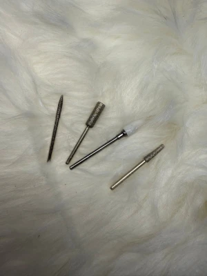 Nagelfilar och slipbits till elfil - Fyra olika slipbits till elfil för naglar, i metall och ett i vitt keramiskt material. Perfekta för att forma, släta ut och ta bort material på konstnaglar. Passar de flesta elektriska nagelfilar. Silverfärgade och i olika former för precision.